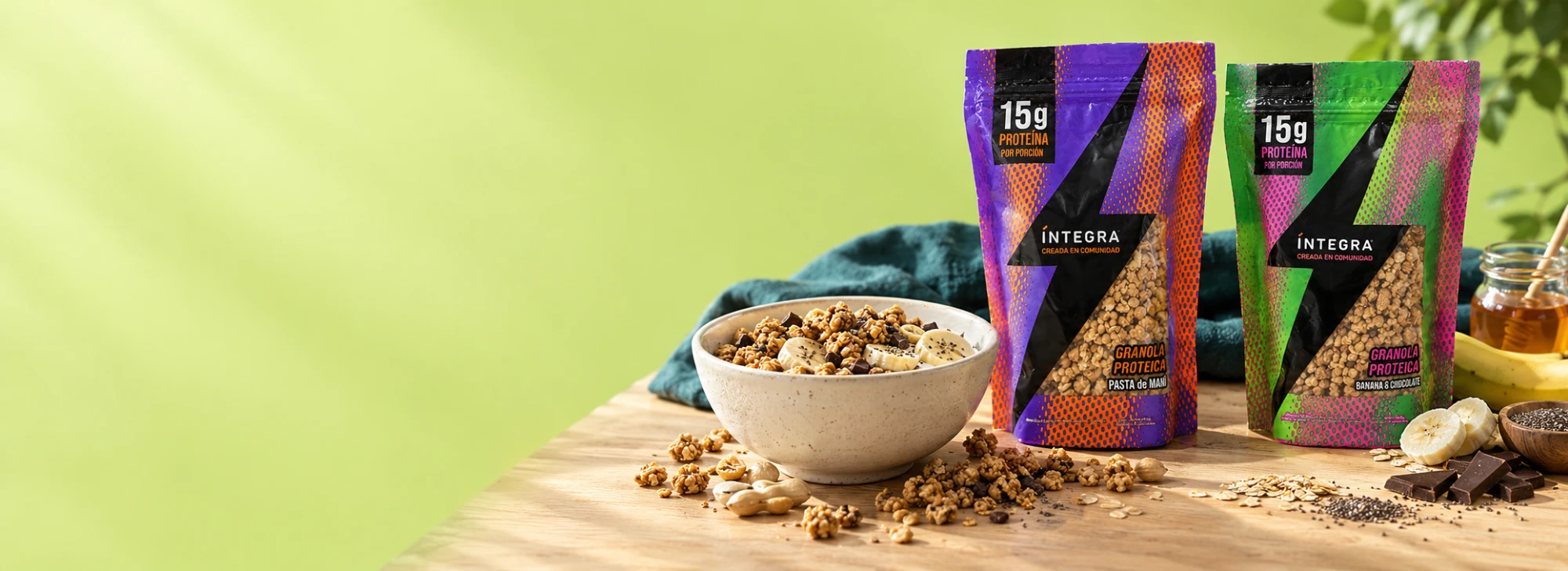 Granolas proteicas Íntegra de pasta de maní y de banana y chocolate, junto a un bowl de granola con banana, miel y chocolate
